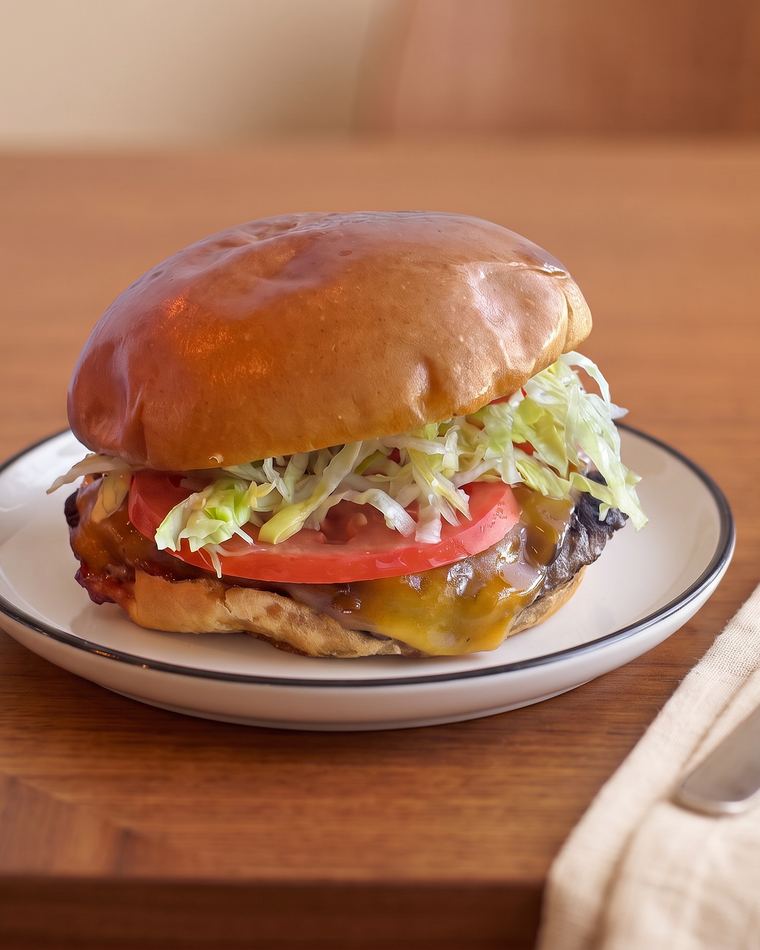 Cheese burger on a brioche bun with melted cheddar, tomato and shredded lettuce